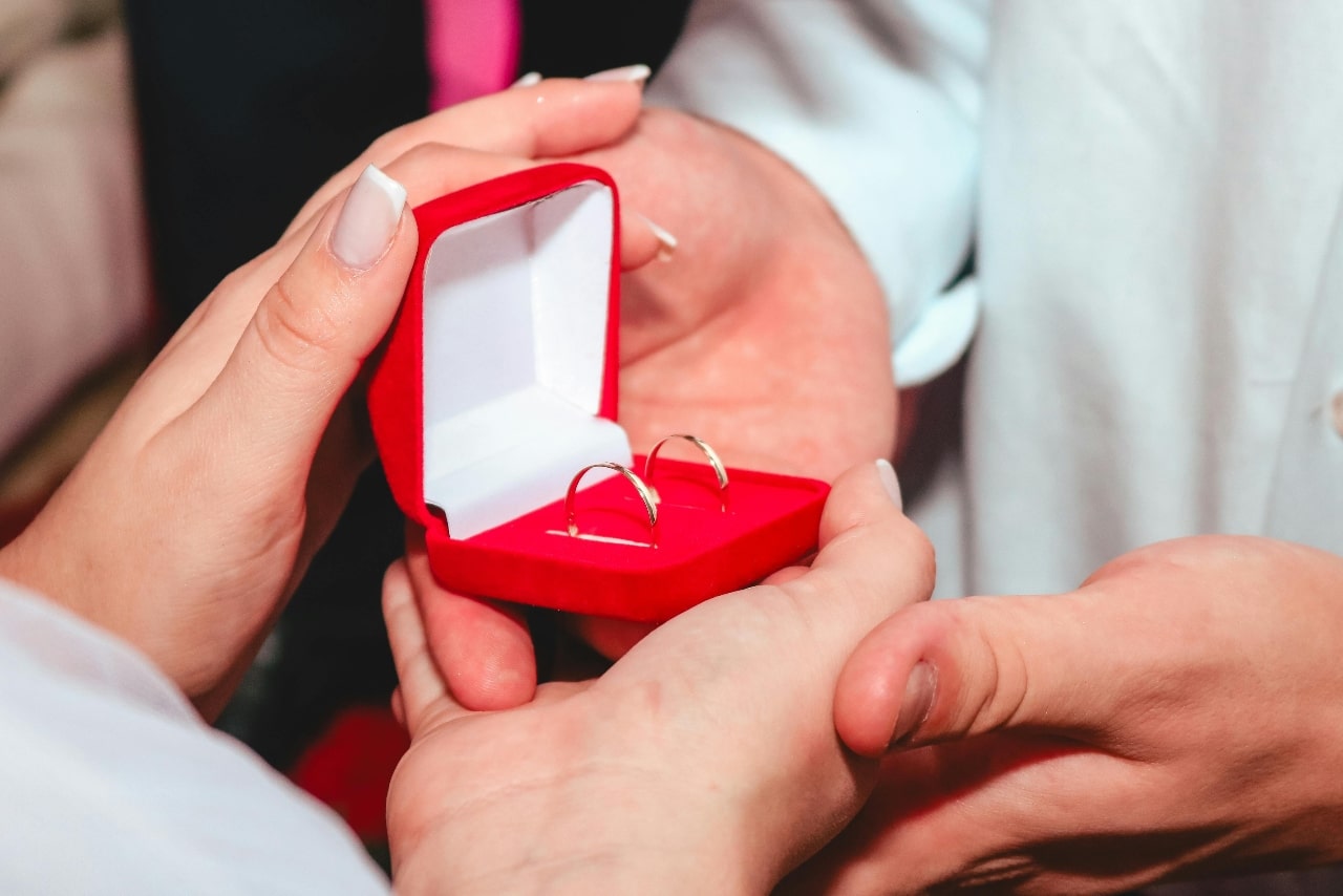 A couple holding a red earring box with golden hoops inside, the woman’s nails nicely manicured.