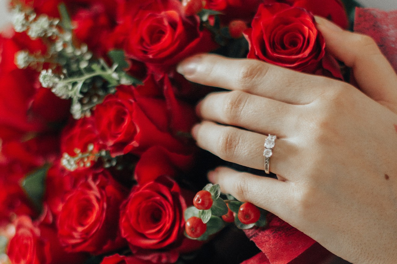 A woman’s hand rests on red roses while wearing a diamond ring.