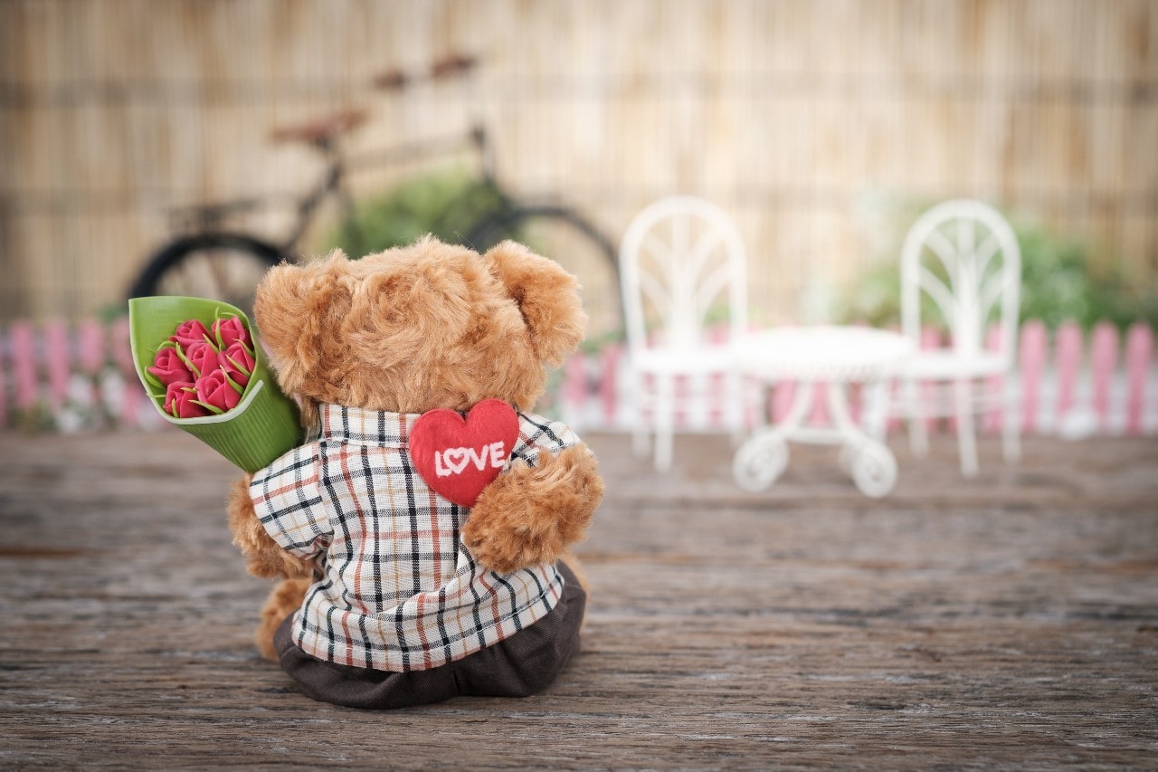 a teddy bear holds a bouquet of flowers and heart in a scene.