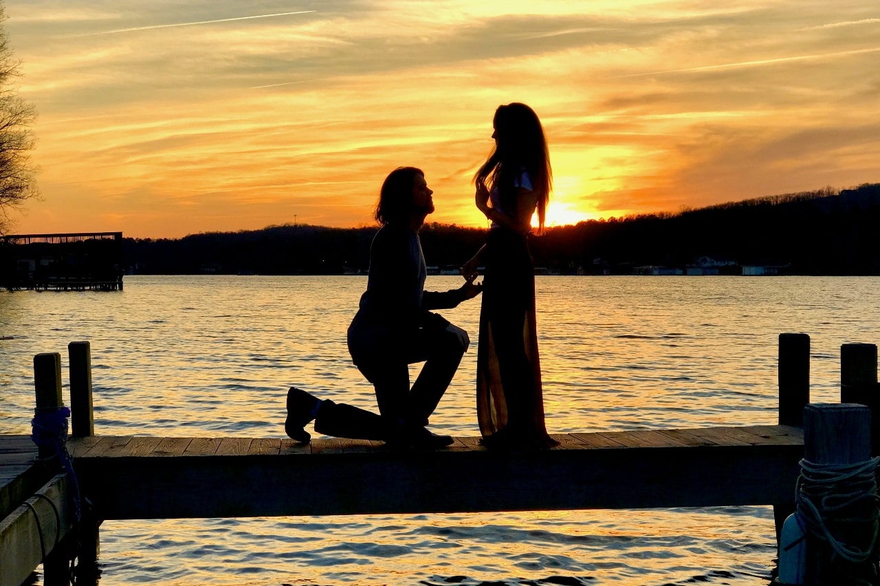a man proposing to a woman on a dock and sunset