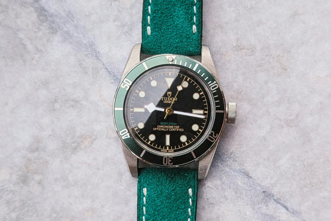 A TUDOR watch with a green strap, rotating bezel, and black dial on a marble surface.