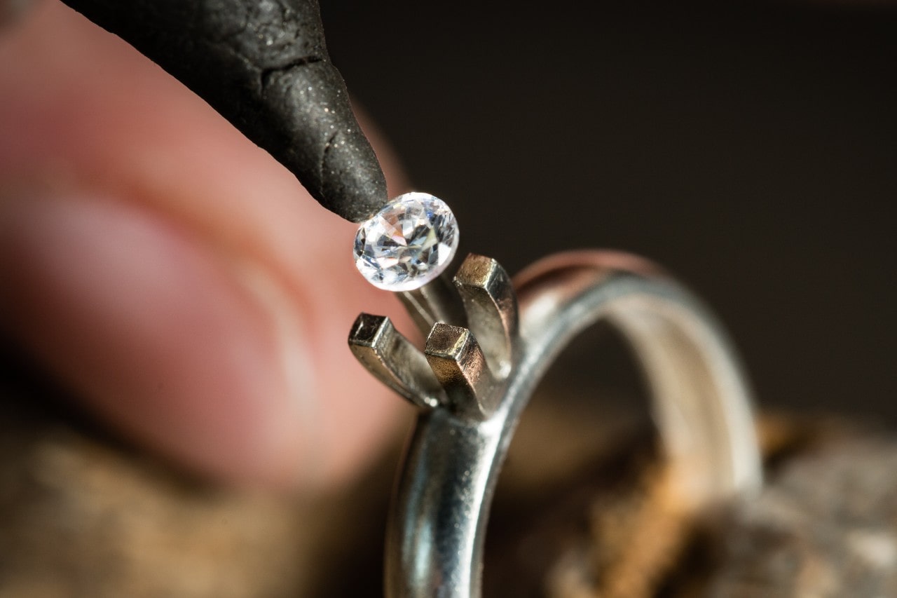 A close up of a jeweler inserting a round diamond into the platinum solitaire engagement ring setting.