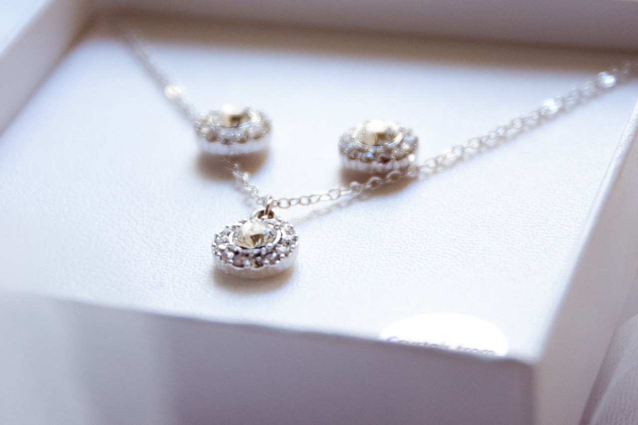A close-up of a set of a diamond pendant necklace and a pair of matching stud earrings displayed in a white jewelry box.
