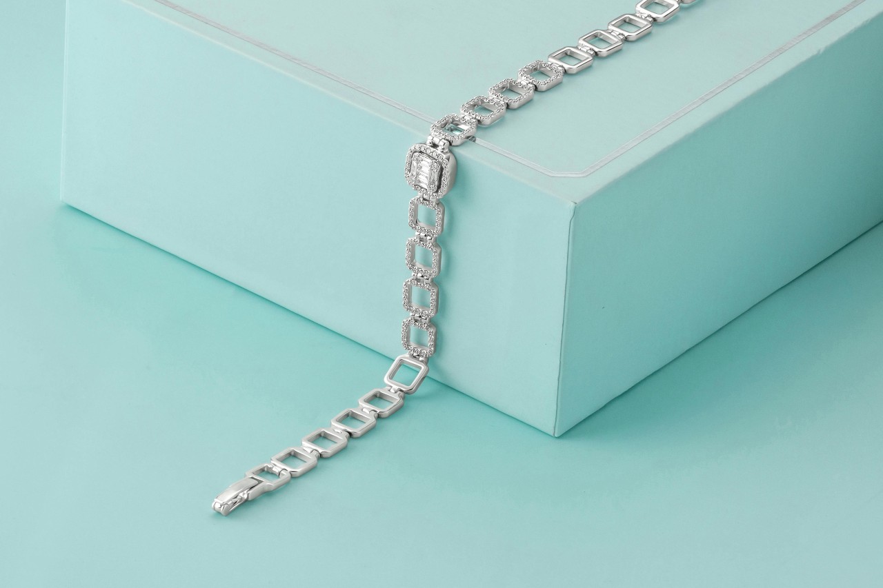 A close-up of a white gold and diamond bracelet with rectangular links elegantly draped over a closed, light blue gift box.