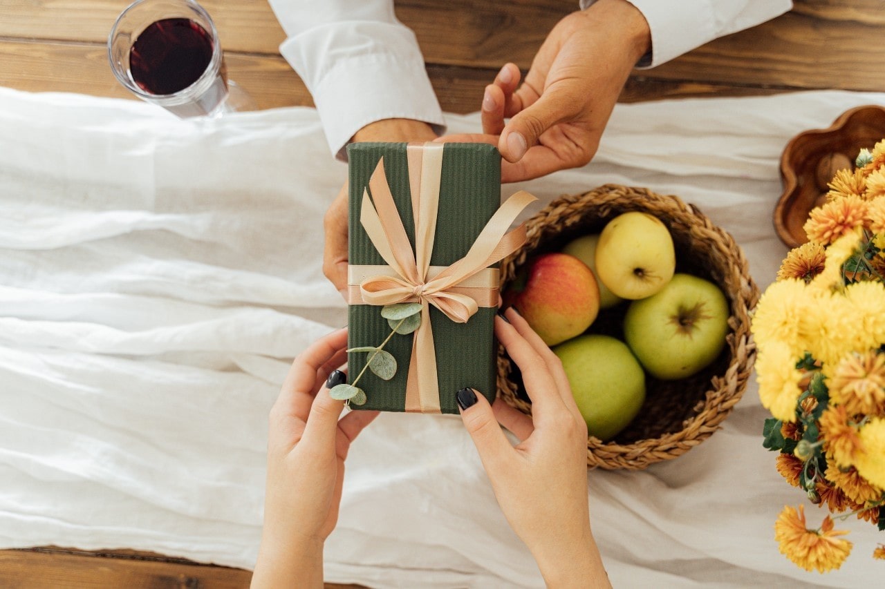 A close up of a person giving a green gift box to another person at a table.
