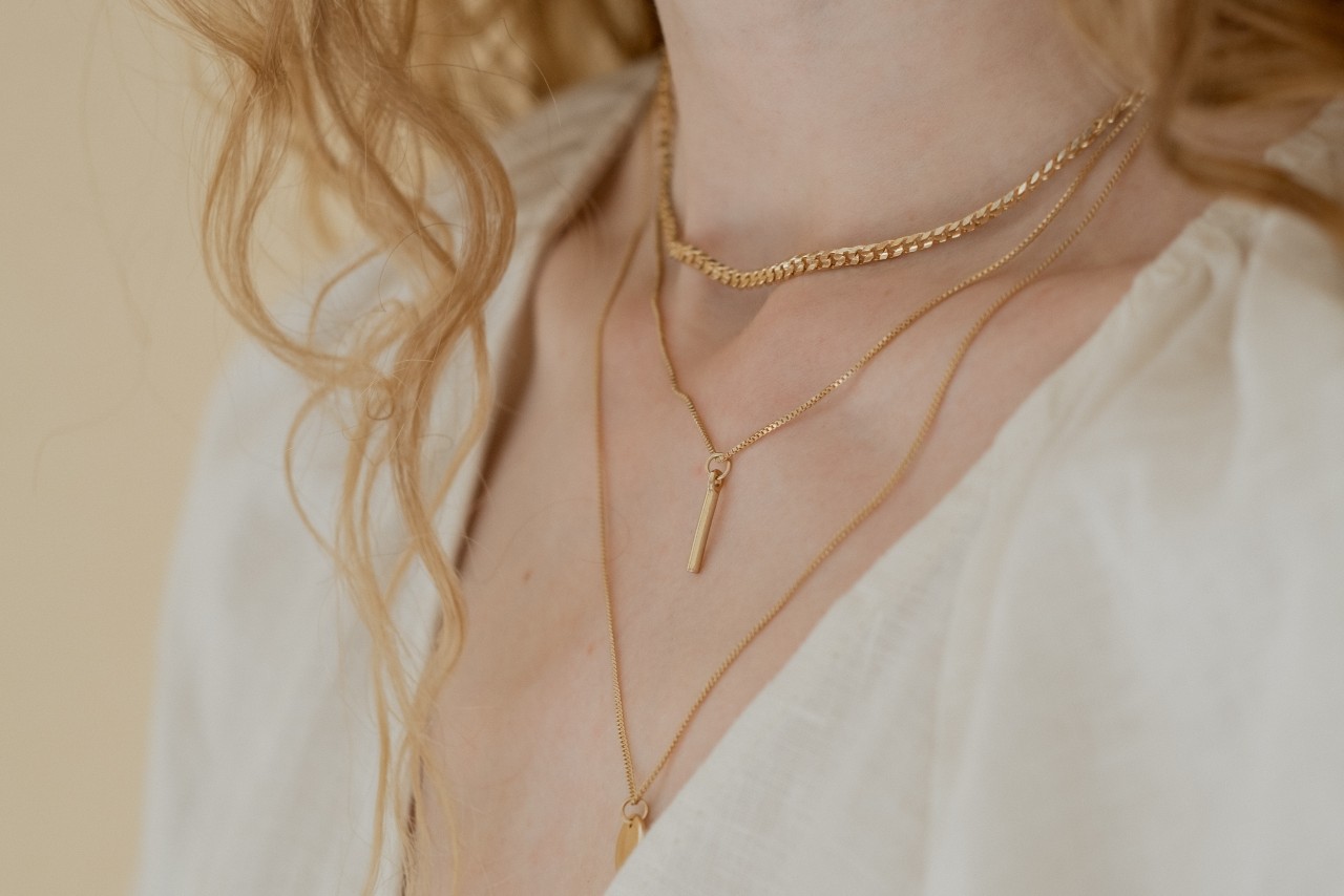 Close-up of a person in a white blouse wearing layered gold necklaces.