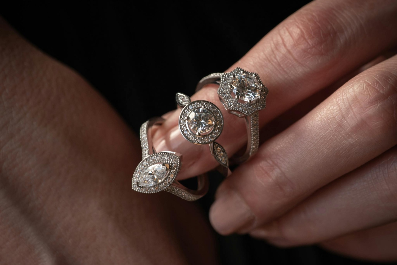 A hand holding three diamond engagement rings with different halo cuts against a dark background.