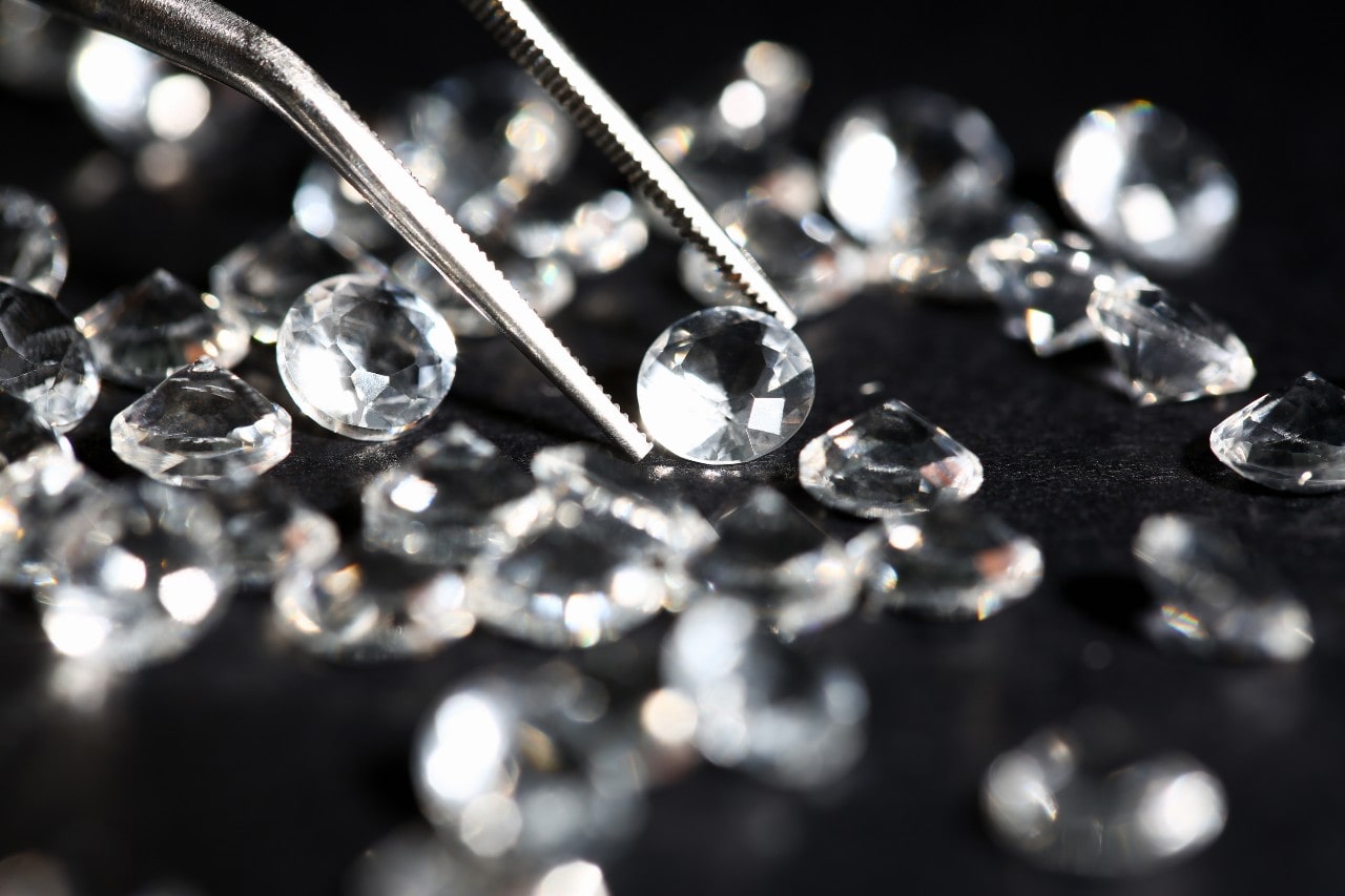 round cut diamonds on a black felt surface with a pair of tweezers picking up one