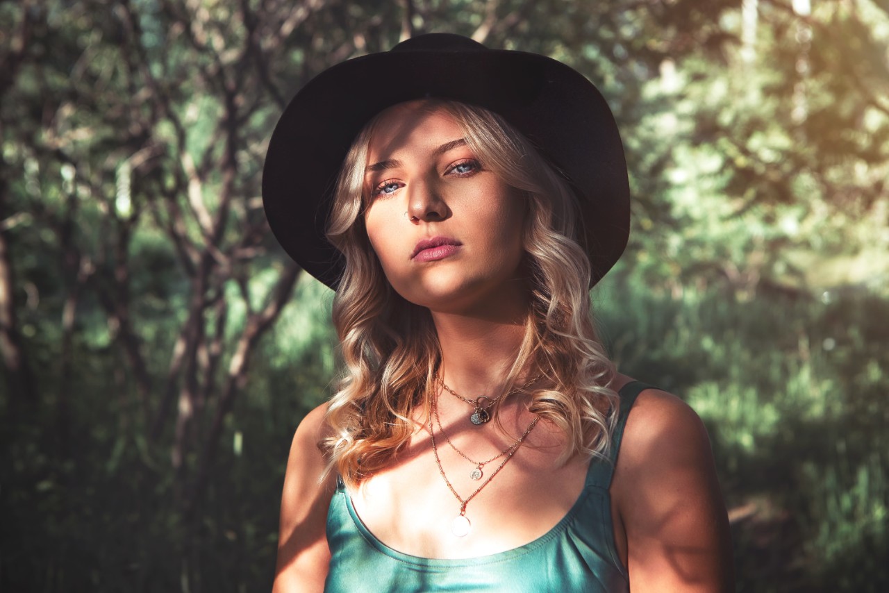 A close up of a woman in sunlight with blond curly hair, showcasing a layered gold pendant necklaces.