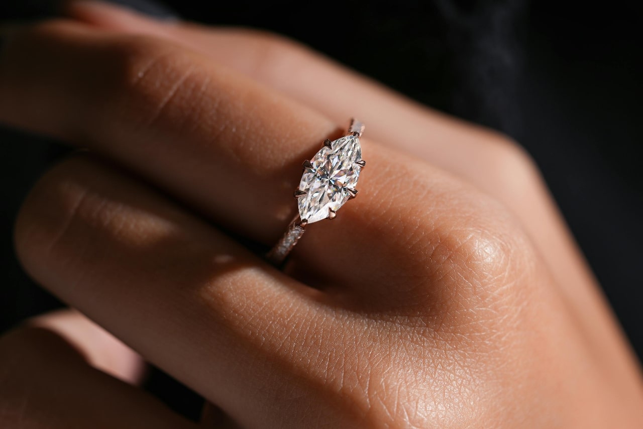A white gold marquise cut diamond engagement ring on a finger.