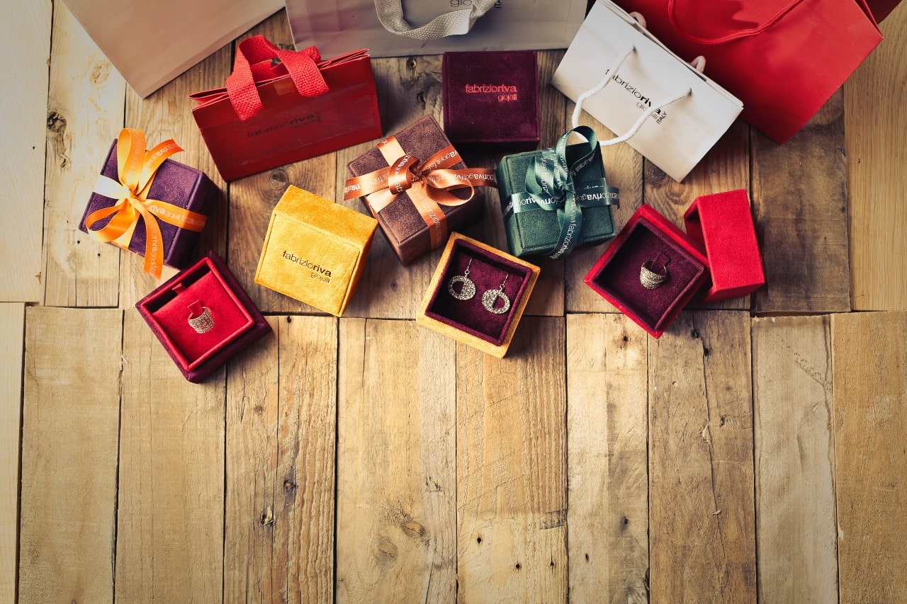 Several velvet jewelry boxes with ribbons scattered around wooden floor, showcasing earrings and rings