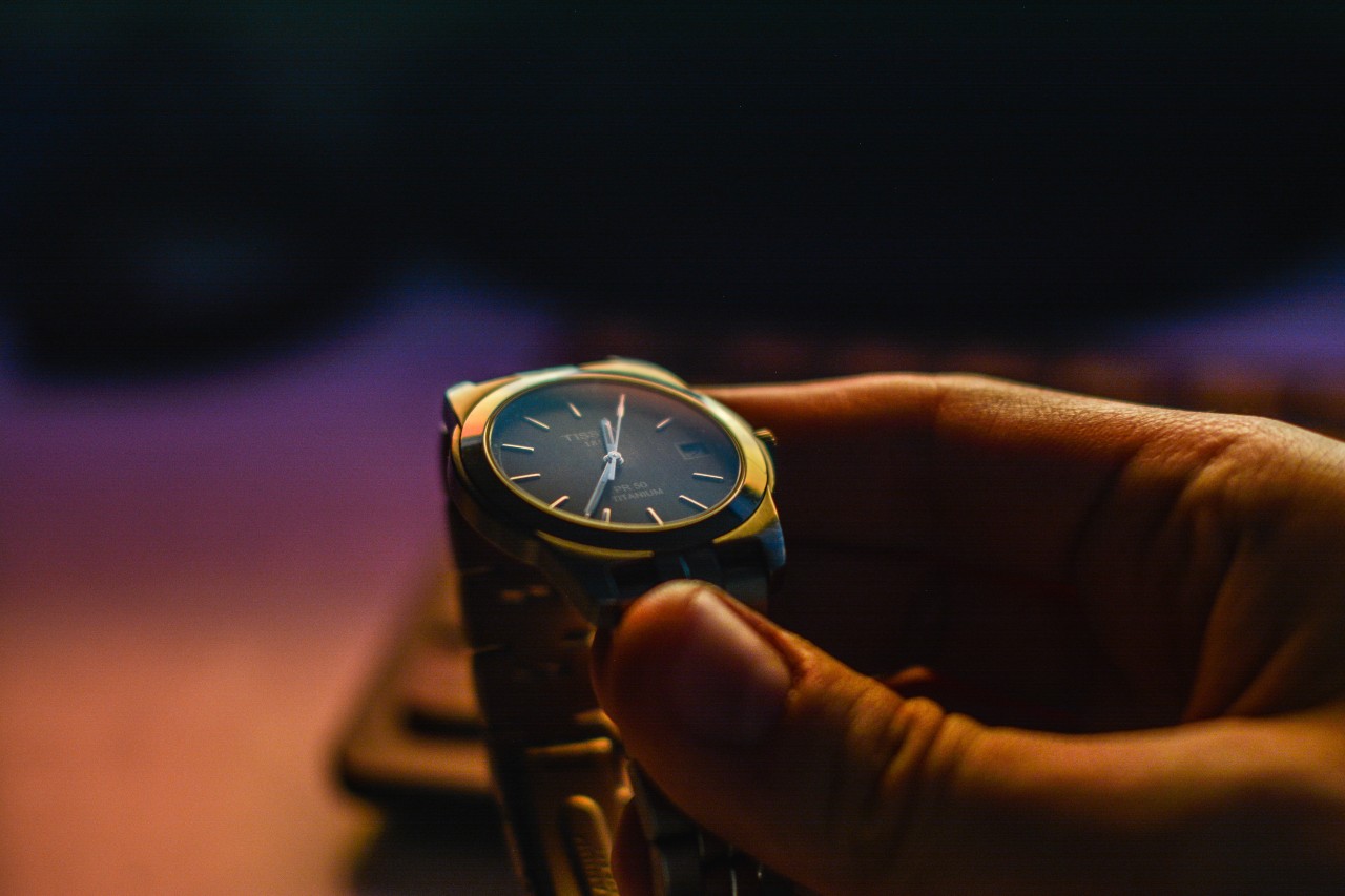 A close-up of a person holding a metallic wristwatch with a deep blue dial.