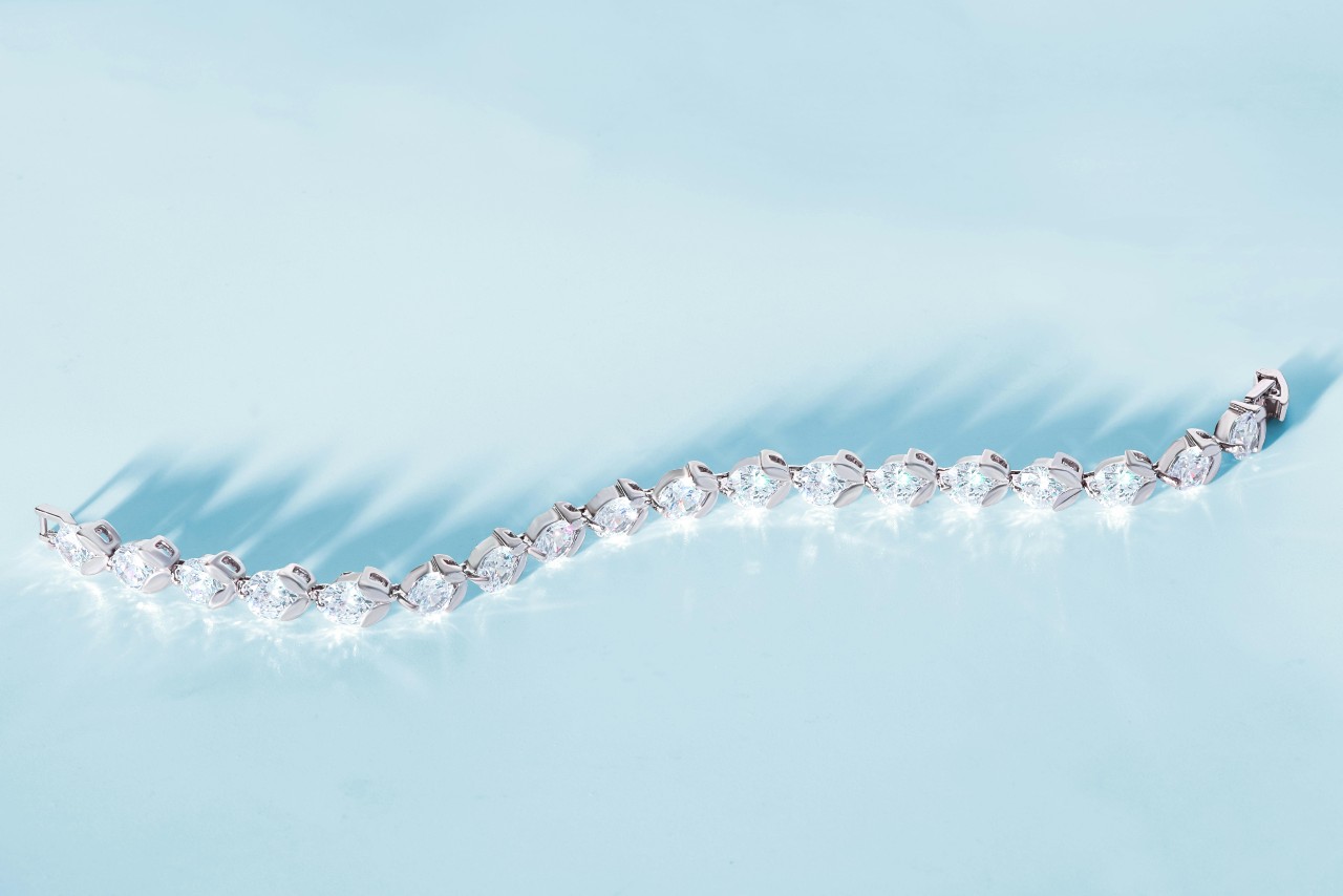 A diamond bracelet resting on a bright light blue surface.