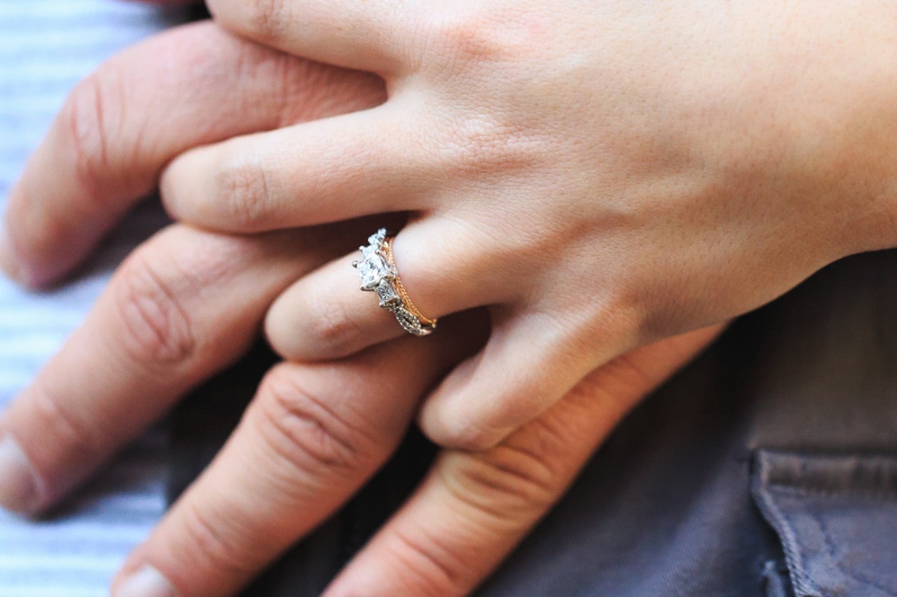 a couple’s hands intertwined, the woman’s hand wearing a mixed metal engagement ring