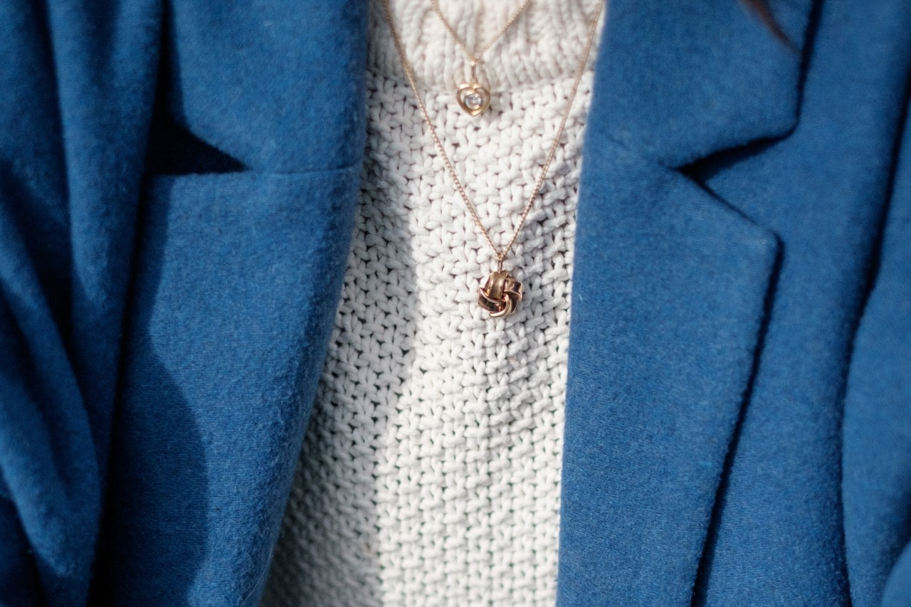 A person wearing a white sweater under a blue wool blazer, with two golden necklaces cascading down the sweater.