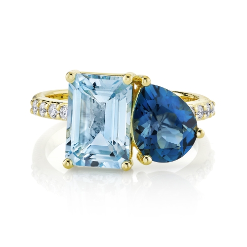 A yellow gold two stone ring with a pear and emerald cut blue topaz adorned with small diamonds