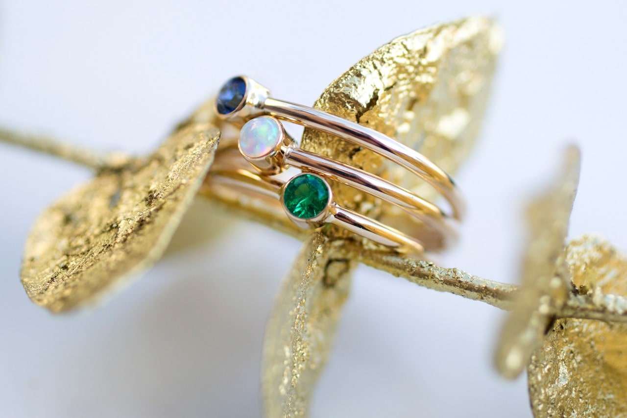 A triple-band yellow gold ring with sapphire, opal, and emerald on gold leaves.