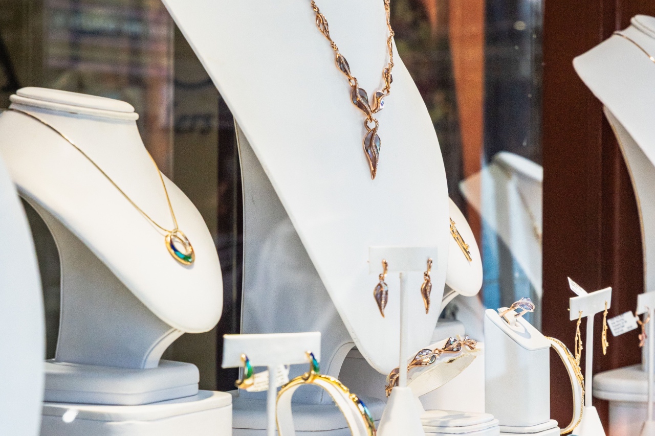 A boutique window display featuring elegant gold jewelry, including an organic leaf-shaped pendant necklace and matching drop earrings on sleek white busts.