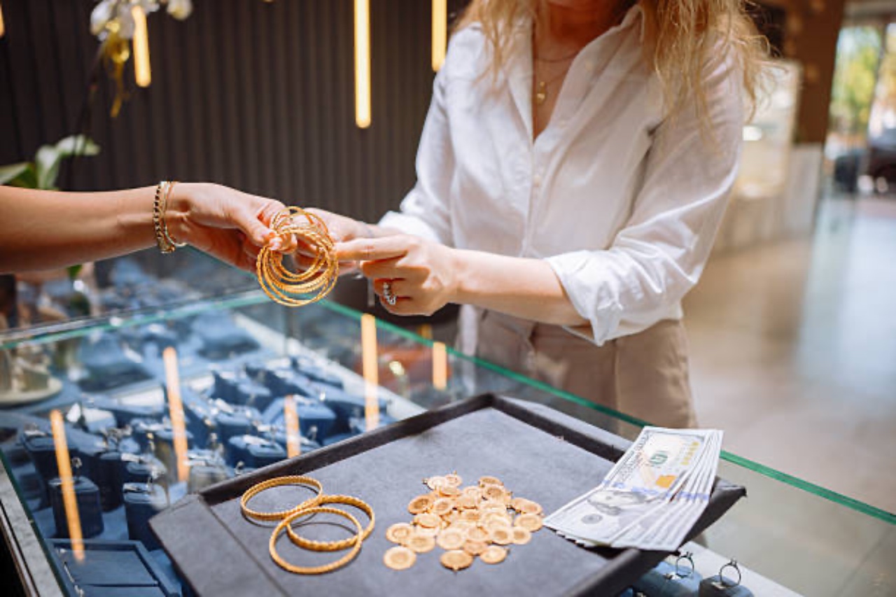 A customer trying on a stack of gold bangle bracelets handed over by a jeweler across a glass display case inside a high-end boutique.