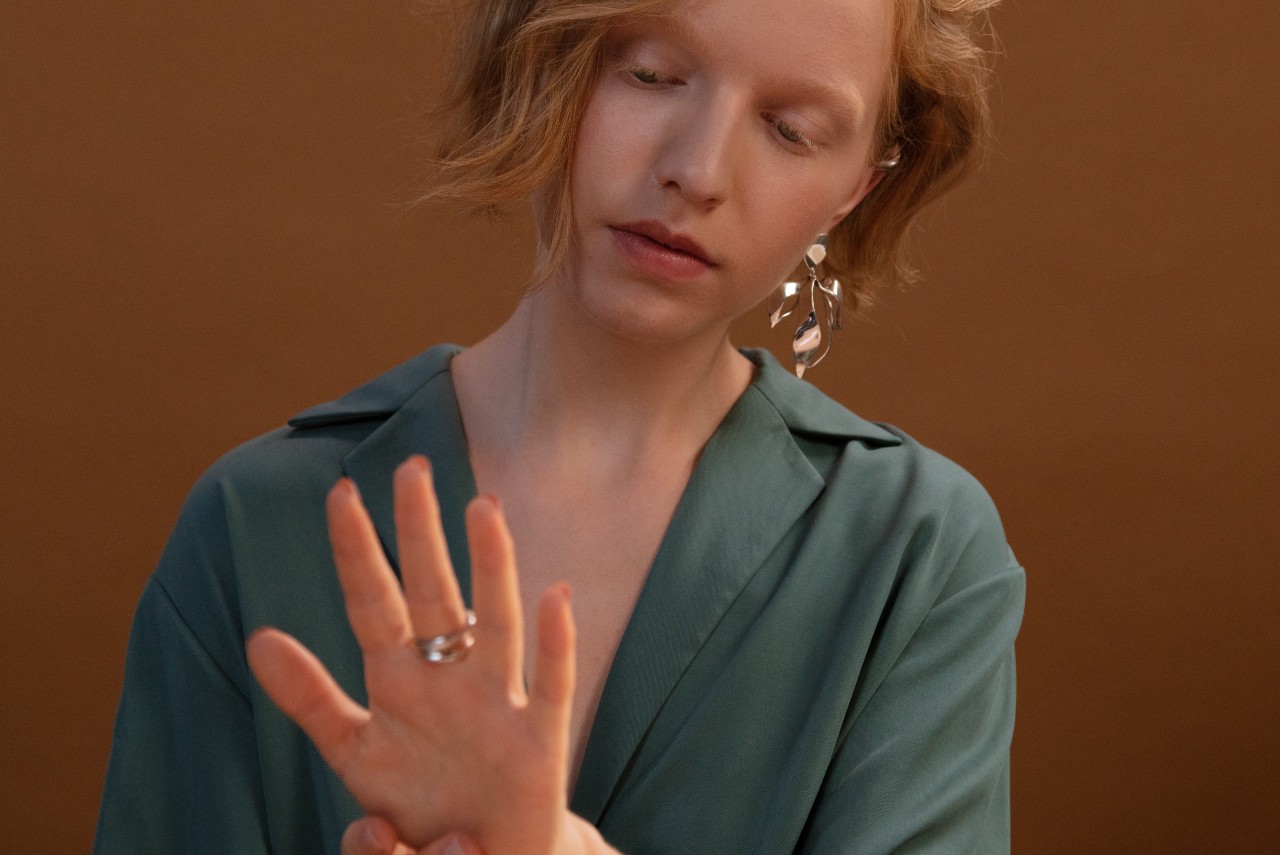 A woman with blonde hair and a turquoise blouse looking closely at the rings on her finger.