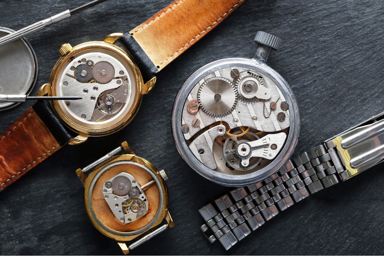 Close-up of three vintage mechanical watch movements on a dark surface, highlighted by gears and cogs.