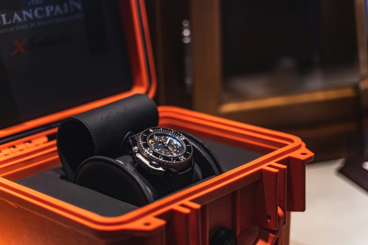 A luxury diving watch with a bold black and silver design sits in an open orange protective case.