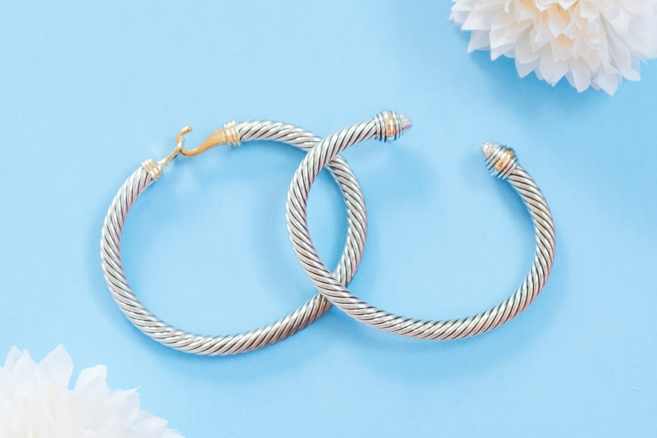 A close up of two silver-toned twisted cable-style bangles displayed on a pastel blue background.
