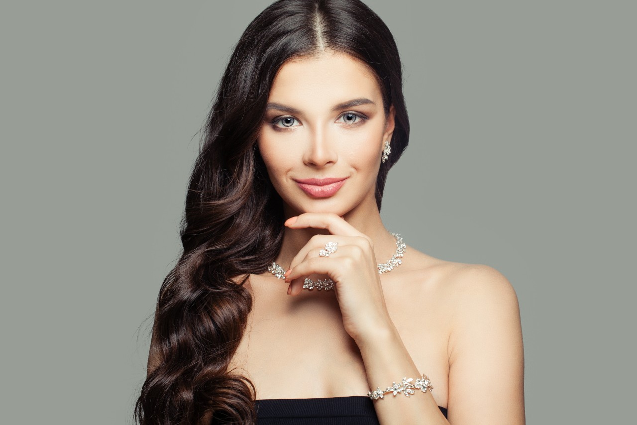 A woman with long brown hair wears elegant diamond jewelry, including a necklace, earrings, and a bracelet.