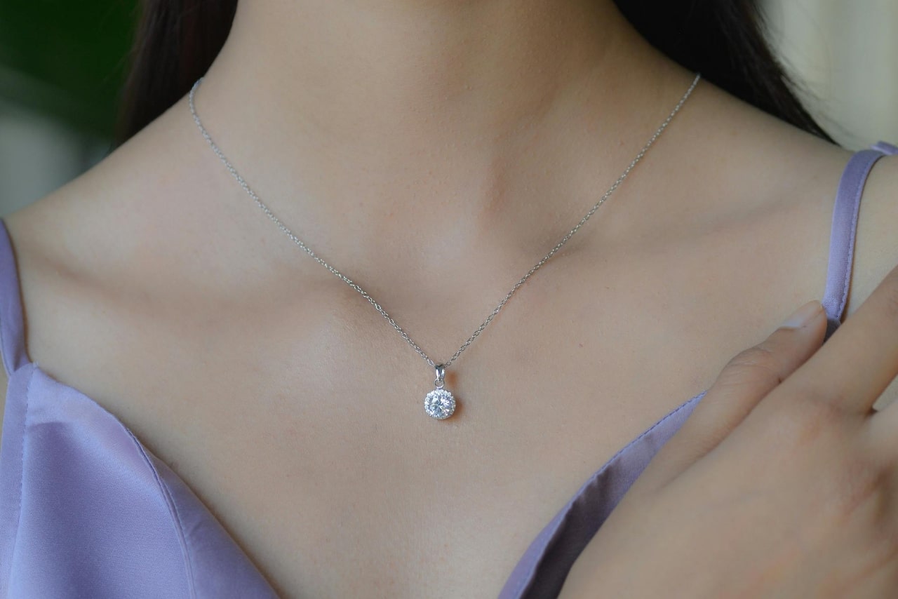 A close-up of a woman's neck adorned with a delicate diamond pendant.