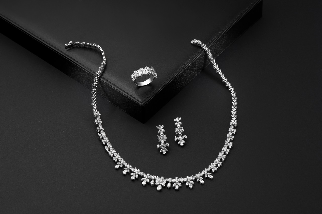 An elegant jewelry set with a diamond necklace, matching earrings, and a ring displayed on a smooth black surface.