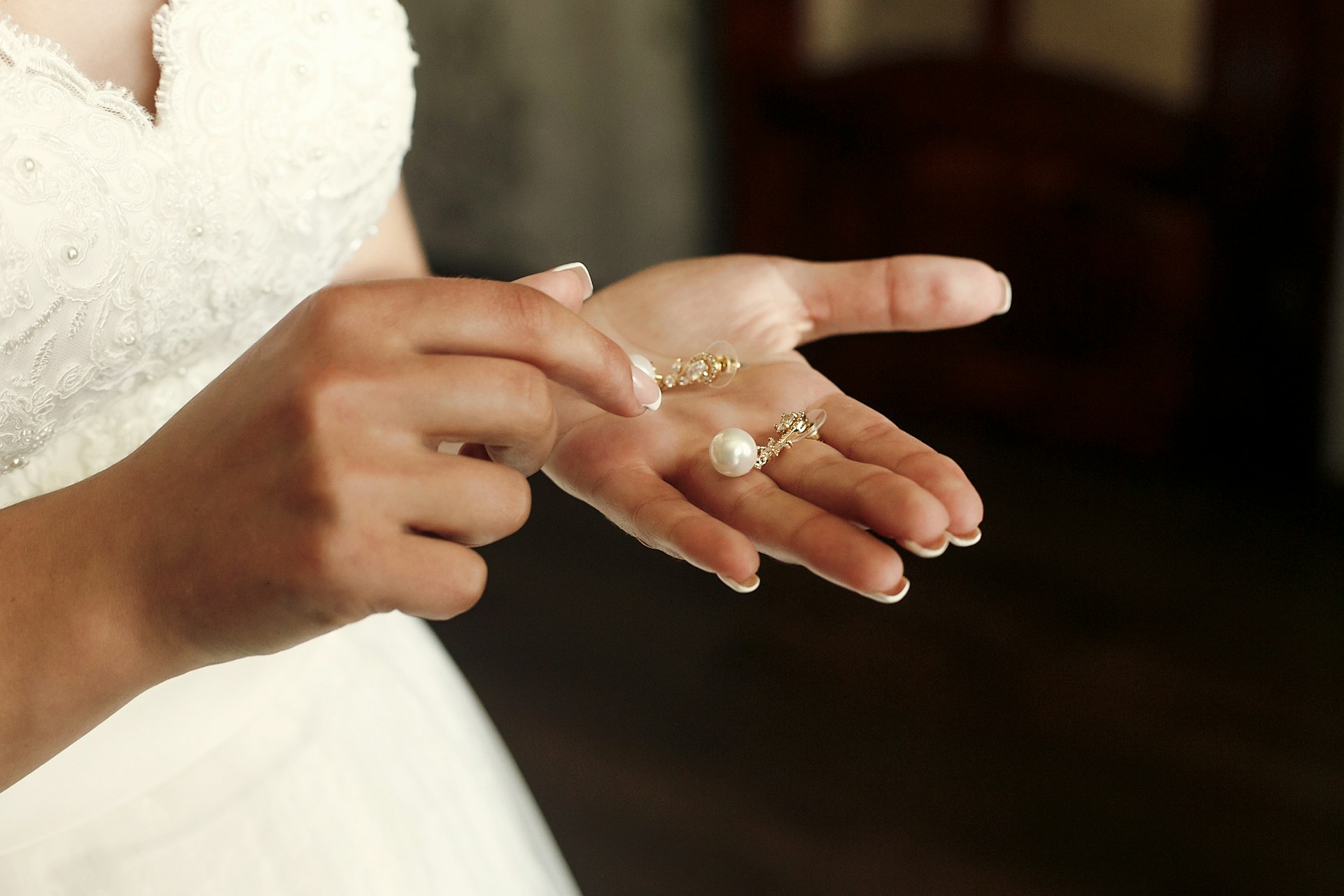 A close up of a bride’s palms with drop pearl earrings on them.