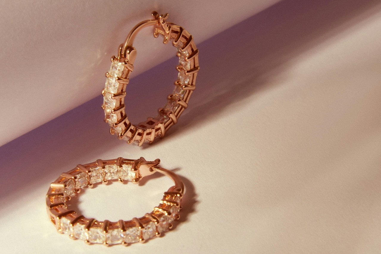 A yellow gold diamond hoops on a beige surface.