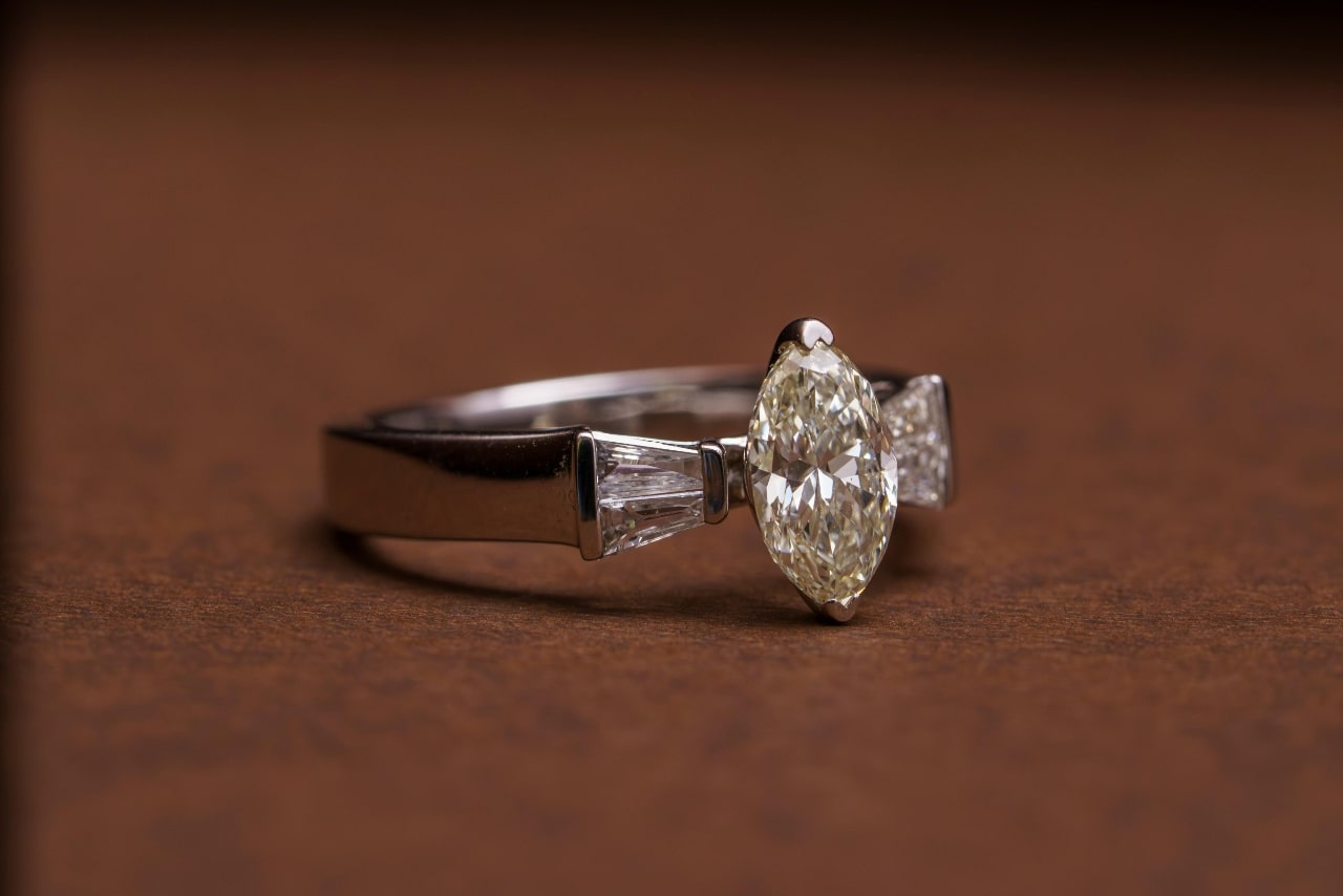 A close up of a three stone engagement ring, laying on brown fabric.