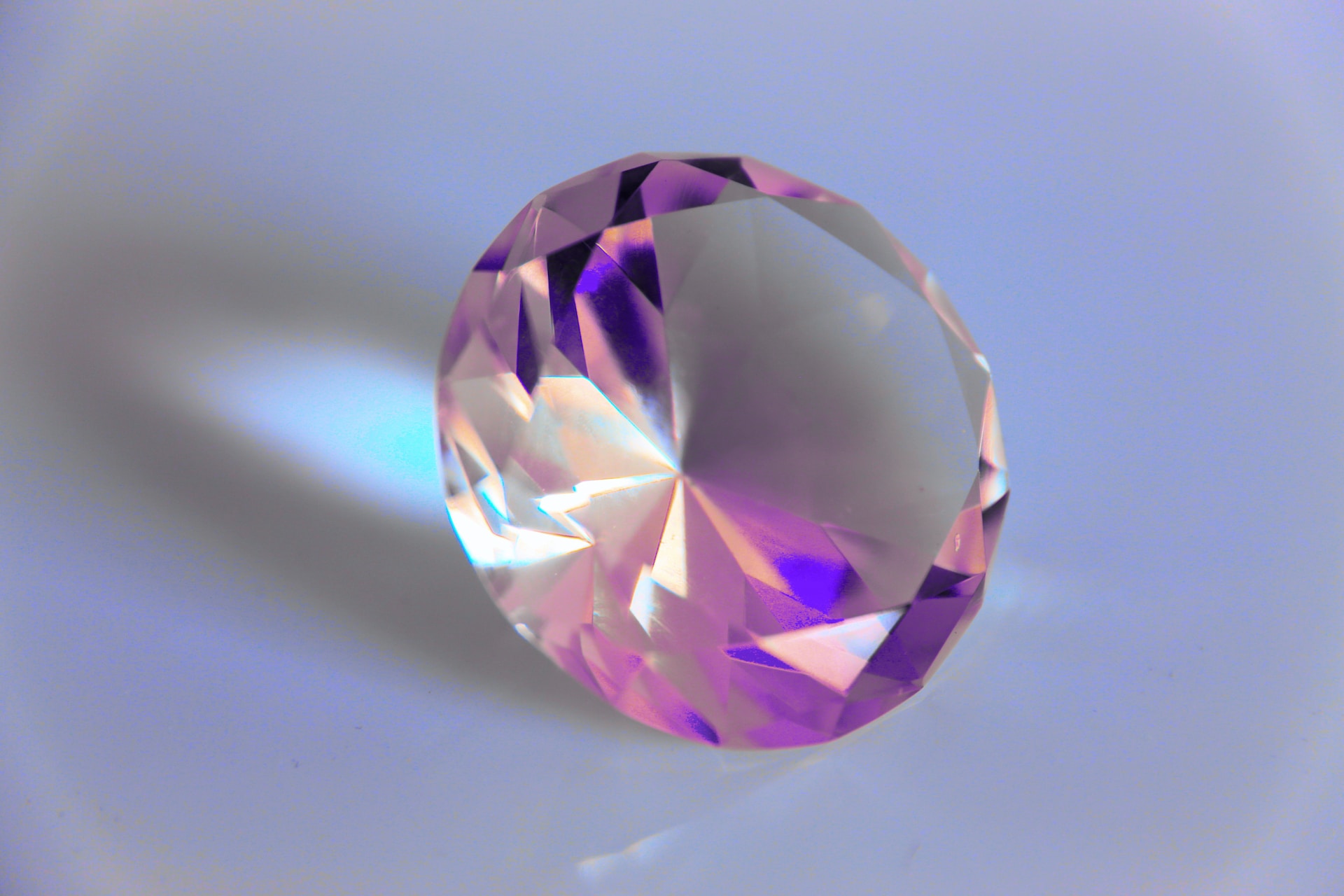 A round, multifaceted gemstone reflects light, casting pink and purple hues. A round, multifaceted gemstone reflects light, casting pink and purple hues.