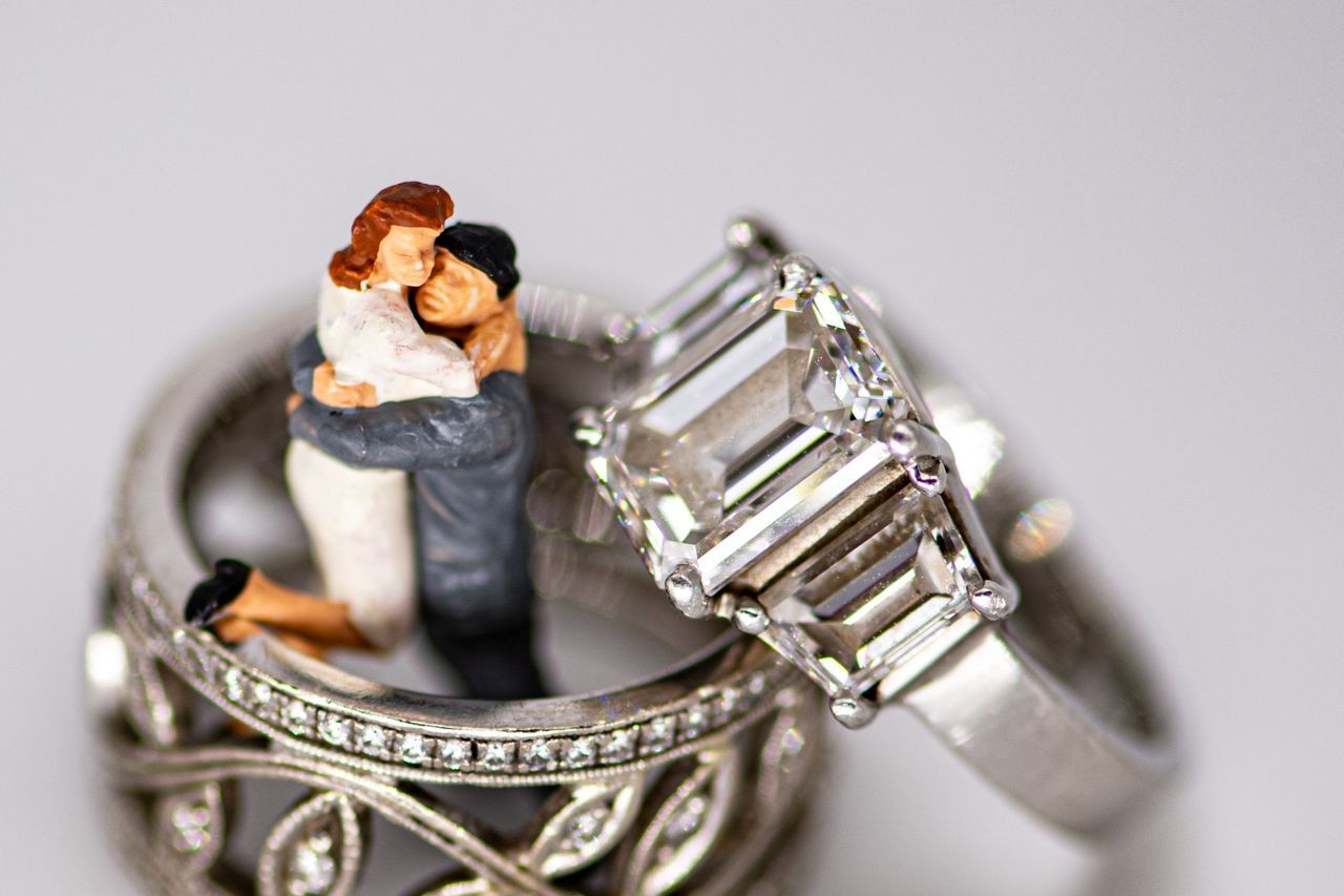A close-up of a white gold wedding set: emerald cut three stone engagement ring and wedding band with intricate floral details.
