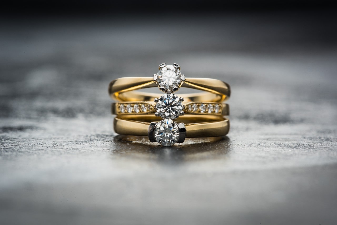 A stack of yellow gold diamond solitaire engagement rings displayed on a textured dark surface, showcasing their sparkling brilliance. A stack of yellow gold diamond solitaire engagement rings displayed on a textured dark surface, showcasing their sparkling brilliance.